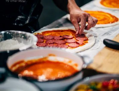 Person putting pepperoni on pizza