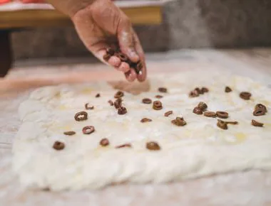 Person putting black olives on focaccia