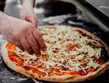 Person putting grated cheese on pizza